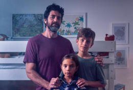 A dad stands huddles with is son and daughter in a child's bedroom